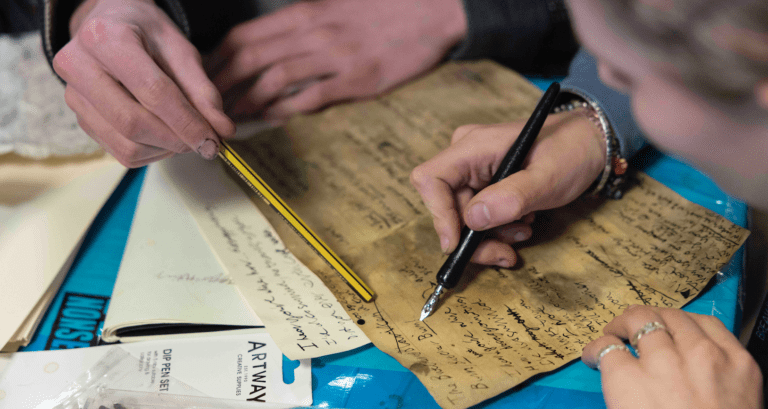 Two participants on the art department course use a caligraphy pen on tea stained paper to create antique documents